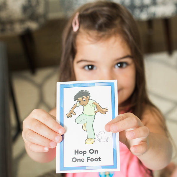Smiling girl holding a Pick n Roll Movez™ Hop On One Foot exercise card during active play